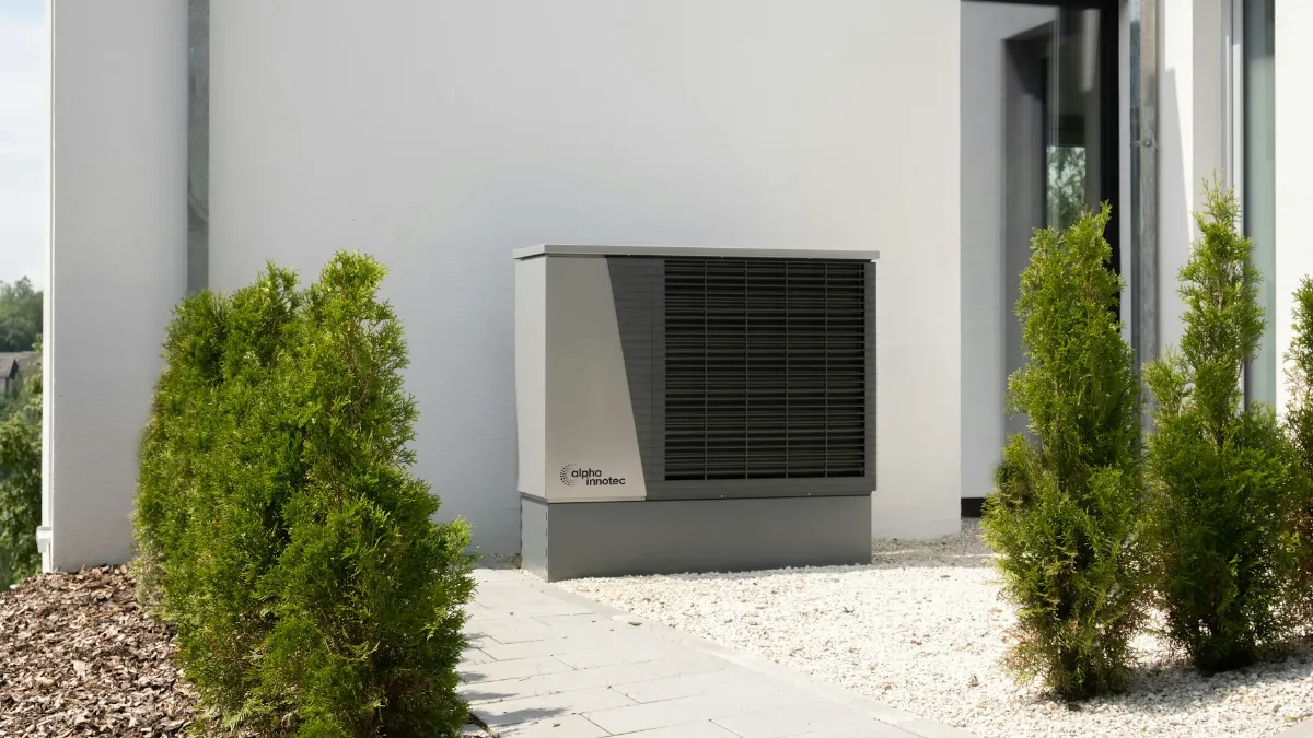 Unité extérieure de pompe à chaleur air-eau posée sur un socle contre la façade d’une maison